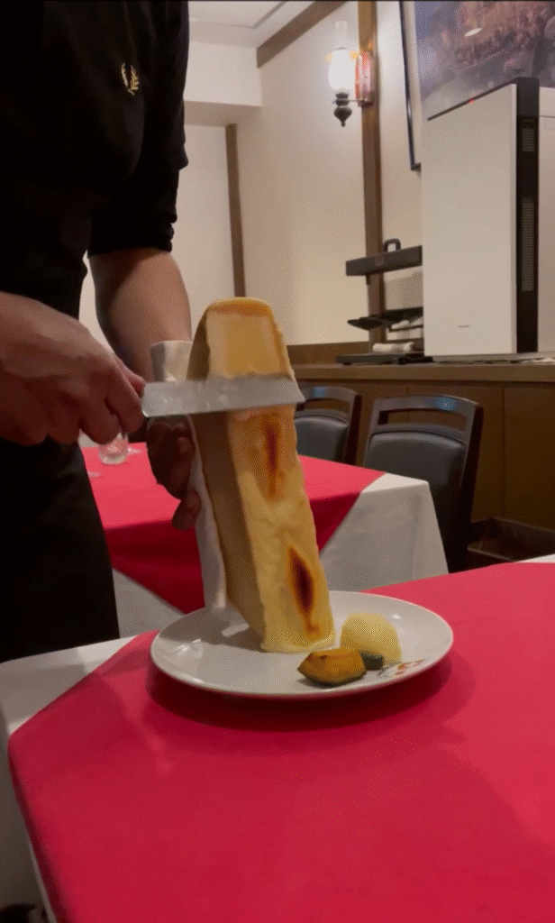 とろけたラクレットチーズを料理にかける様子