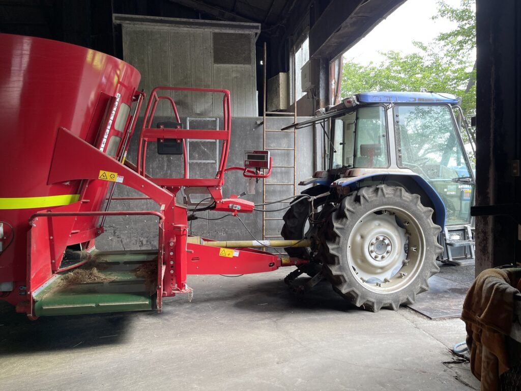 トラクターでTMRミキサーを牽引し牛に餌を配る酪農の給餌作業